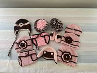 Nine pieces including diaper covers, hats with various decorations, and booties in pink and brown crochet yarn