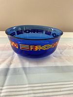 Side view of blue glass bowl showing multicolor international flags motifs around its circumference.