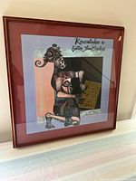 Full view of the framed Cameroonian art print showing the abstract African figure in earthy tones inside a wooden frame with glass.