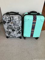 Photo showing two hard-shell carry-on suitcases side by side on a grey carpet. The left suitcase is patterned in black and white with travel landmarks and the right suitcase is turquoise with a multicolored vertical textile strip.