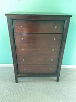 Front view of dark brown wooden dresser with five drawers and round metal knobs.