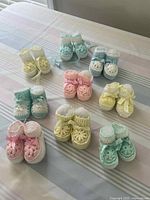Nine sets of crocheted baby booties in assorted pastel colors arranged on a table.