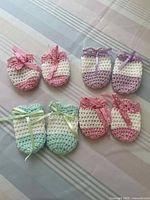 Four pairs of crocheted baby mittens in pastel shades with ribbons displayed on striped fabric background