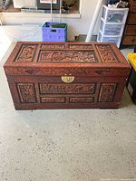 Front view of the wooden trunk showing hand-carved panels, lock, and feet.