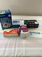 Wide shot showing 8 sealed health test kits and 1 boxed blood pressure monitor arranged on white surface.