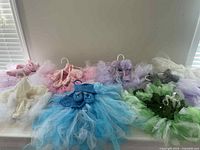 Nine infant tutu outfits arranged on hangers showing the various colors and matching accessories including headbands and booties.
