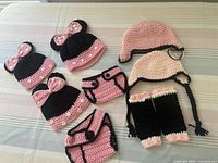 Nine-piece crocheted clothing set arranged showing hats, diaper covers, and leg warmers in pink and black with Minnie Mouse theme.