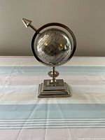 Front view showing mounted silver metal globe on pedestal base with arrow meridian ring and engraved map details.