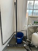 Mop with metal and plastic handle, blue bucket and white fan in corner of room