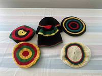 Photo showing six multi-colored crocheted hats laid out on a striped surface, displaying round and beanie styles with bold color stripes and circles.