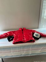 Red puffer jacket with two hats on table under window light