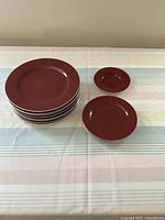 Eight plates displayed; seven larger plates stacked and one small plate beside them on a striped tablecloth.