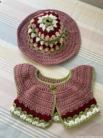 Crocheted strawberry shortcake style hat and capelet displayed on a flat surface.