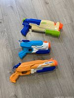Three Nerf Super Soaker water blasters laid on wood floor