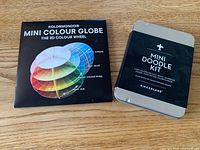 Front view of sealed Kolormondo mini colour globe box and closed Kikkerland mini doodle kit tin