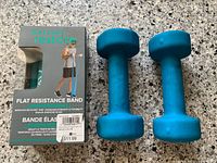 Two blue 5 lb dumbbells beside boxed Gaiam flat resistance band