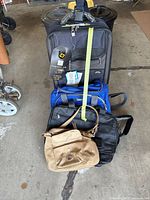 Photo showing the four bags stacked: black wheeled luggage, blue toiletry bag, black leather satchel, and tan leather purse on top.