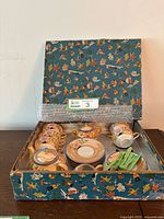 Full set of items arranged in original open box showing tea set and cutlery.