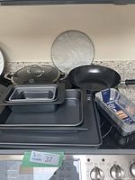 All cookware and bakeware pieces arranged on a countertop showing frying pans, lids, baking and cake pans