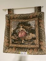 Full view of the wall hung tapestry showing the young girl in a pastoral setting with sheep and a hay cart, bordered by decorative leaves and floral patterns. The tapestry is hung on a rod.