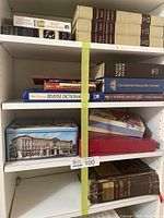 Shelf with multiple hardcover and softcover books including dictionaries and a tin box with stamps.