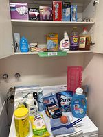 Photo of open cabinet shelf with boxed Philips brand light bulbs and various spray and liquid cleaning products beneath