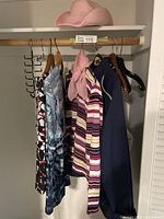 Long sleeve ladies T-shirts and navy blue jacket hanging on wooden hangers inside a closet rod.