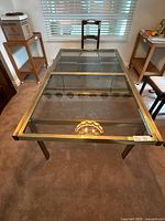 Front angled view showing the clear glass top, metal frame, and visible expansion leaf against a carpeted floor.