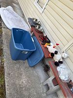 Photo showing blue Sterilite plastic storage bin and lid, dog bed partially visible placed nearby, dog bowls, retractable leash, harness, dog toys and other accessories on bench.