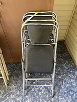 Four stacked vintage metal folding chairs with black vinyl seats and backrests, chrome frames.