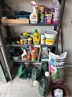 Image of metal shelving with assorted gardening tools, chemicals, sprays, soil bag, and watering cans of various sizes.