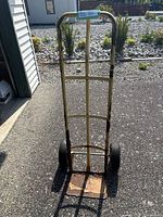Front view of yellow painted metal hand dolly with rubber tires, showing wear and rust on base plate and frame.