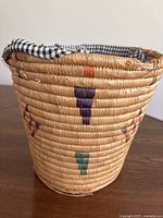 Close-up of Indigenous hand woven basket showing fabric lining, colored geometric patterns, and rim damage