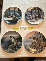 Four wolf-themed collector plates arranged on a table showing different natural scenes including snow and forest, nice variety of wolf poses and environments.