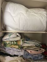 White quilted comforter and collection of folded various linens with floral and botanical patterns and pastel colors