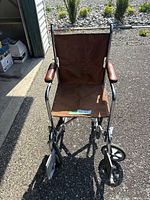 Front view of a brown transport wheelchair with metal frame, vinyl seat and armrests.