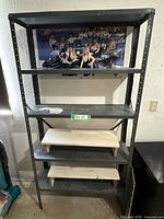 Front view of the entire 5-shelf metal shelving unit showing 3 metal shelves and 2 wooden shelves. Visible signs of use and a poster on the wall behind.