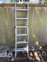 Front view of the ladder standing against a wooden fence on cinder blocks, showing the rungs and A-frame design.