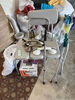 Overall image of the lot showing shower chair, raised toilet seat, cane, vaporizer box, hand picker, and suction handles.