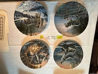 Four Kevin Daniel ceramic decorative plates with wolf/wildlife scenes, top view showing details of the plates