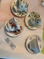 Four fine china teacups and matching saucers with floral prints and gold trim laid on a white cloth