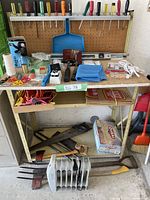 Tool bench with assorted hand tools including screwdrivers, saws, axes, scissors, ropes, and other accessories.