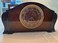 Front view of vintage Seth Thomas mantel clock with dark wood case and round clock face covered by glass and gold-tone bezel.