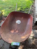Red steel wheelbarrow tray with visible wear and rust, showing a partially torn label indicating 4 cubic feet capacity.
