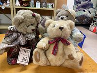 Three teddy bears on table showing overall condition and clothing details