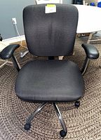 Front view of black fabric swivel office chair showing seat, back, armrests, and chrome base with casters