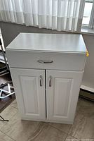 Front view of white laminate cupboard showing drawer, double doors, and handles