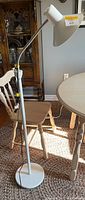 Full view of white adjustable floor lamp standing beside table and chair