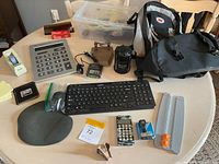 Entire lot on tabletop showing backpack, keyboard, mouse, calculators, bin with cables and various desk accessories