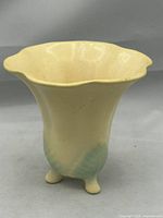 Front view of the 1930s American pottery vase with scalloped rim and tripod feet showing matte yellow glaze and pale green highlights near the base.